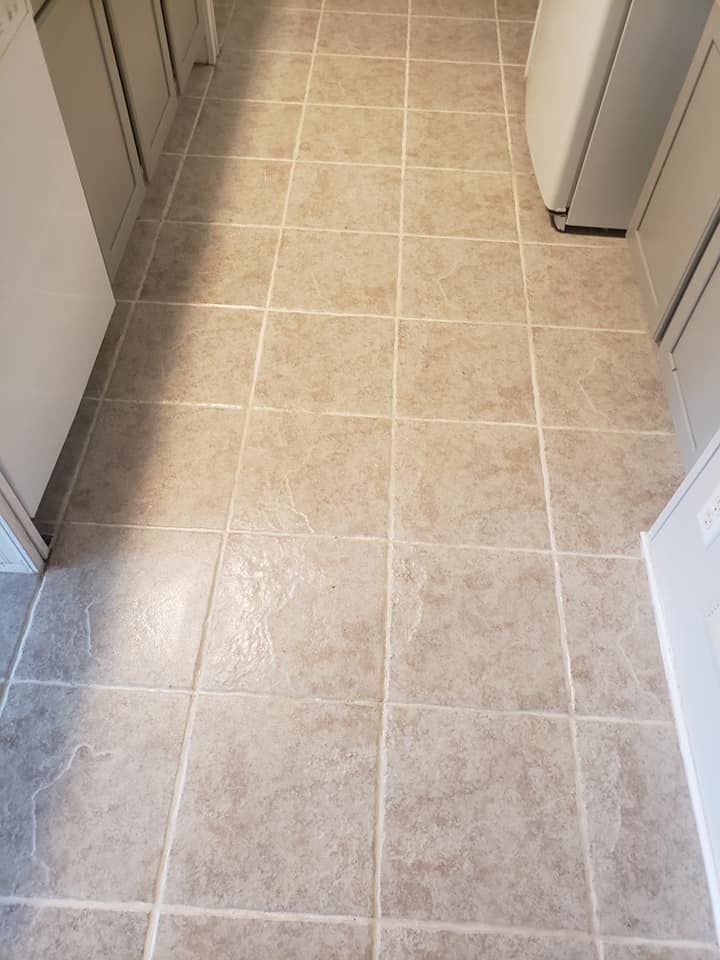 A kitchen floor featuring light tan, square-tiled vinyl flooring running between white cabinets and a laundry appliance.