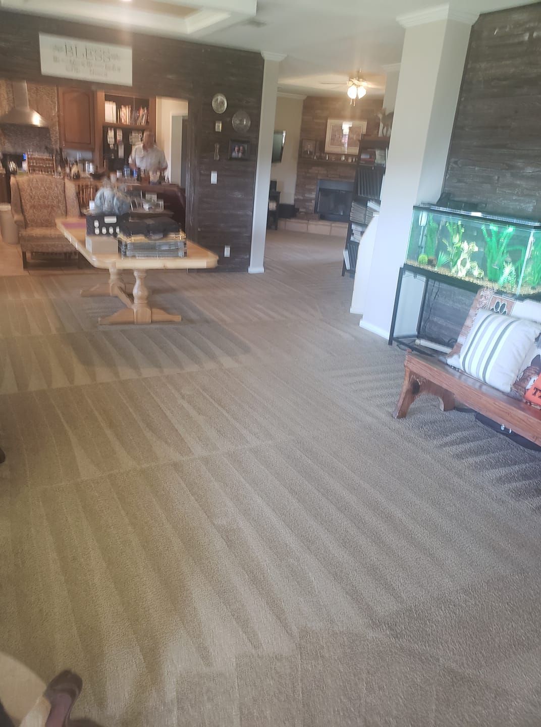 A spacious home interior with tan carpet featuring vacuum lines, a long wooden dining table, and a fish tank on a stand.