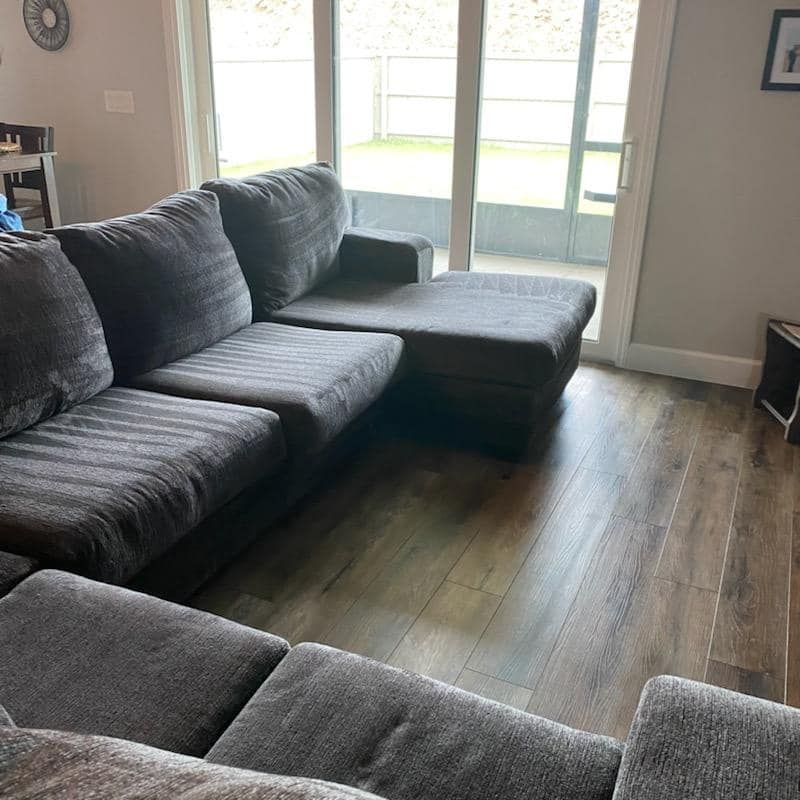 A dark gray sectional sofa sits in a living room with wood-look flooring and a glass sliding door.