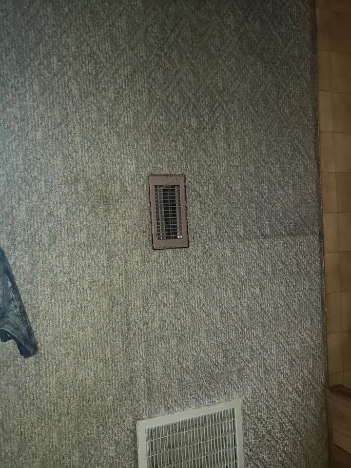 A grey textured wall with a small vertical HVAC vent and a larger white rectangular return air grille below it.