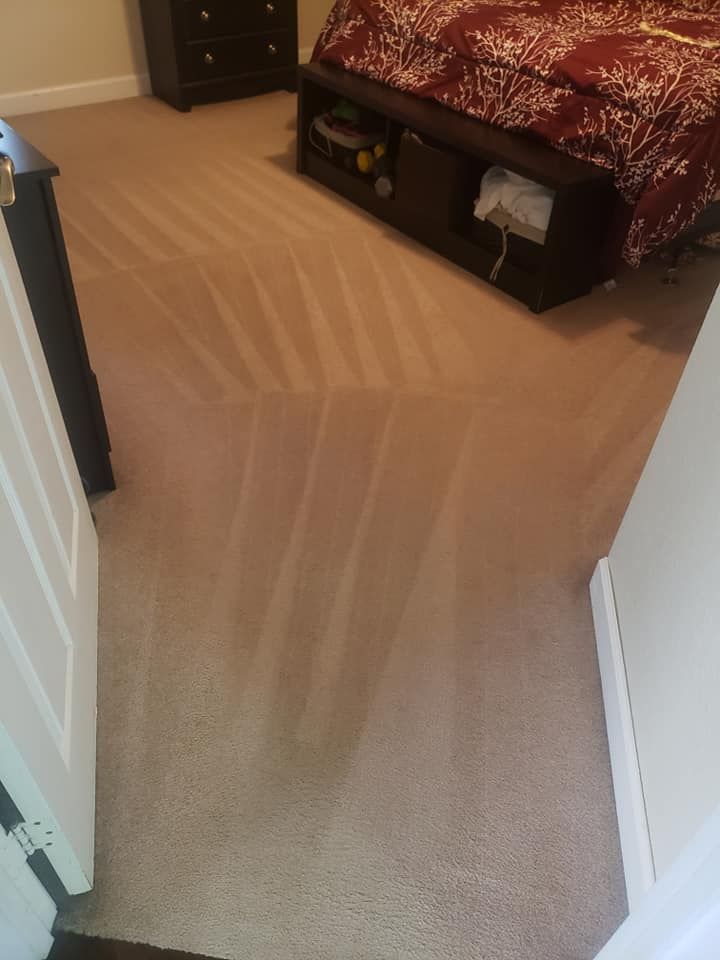 A bedroom with tan wall-to-wall carpet featuring fresh vacuum tracks, a dark wood bed frame, and a matching dresser.