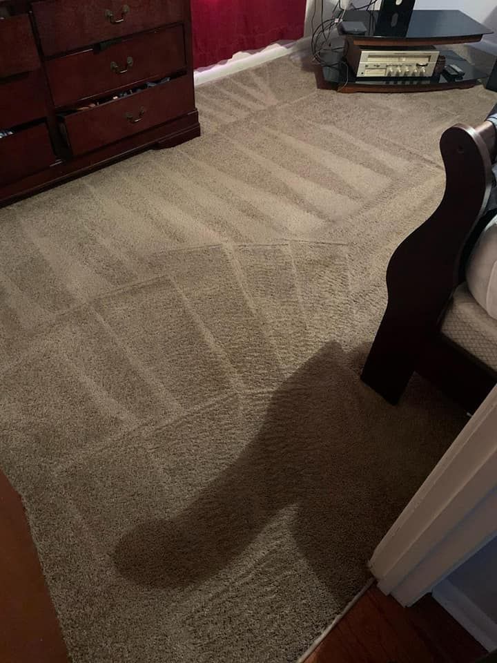 A freshly vacuumed beige carpet showing distinct parallel lines, next to a dark wood dresser and a piece of furniture.