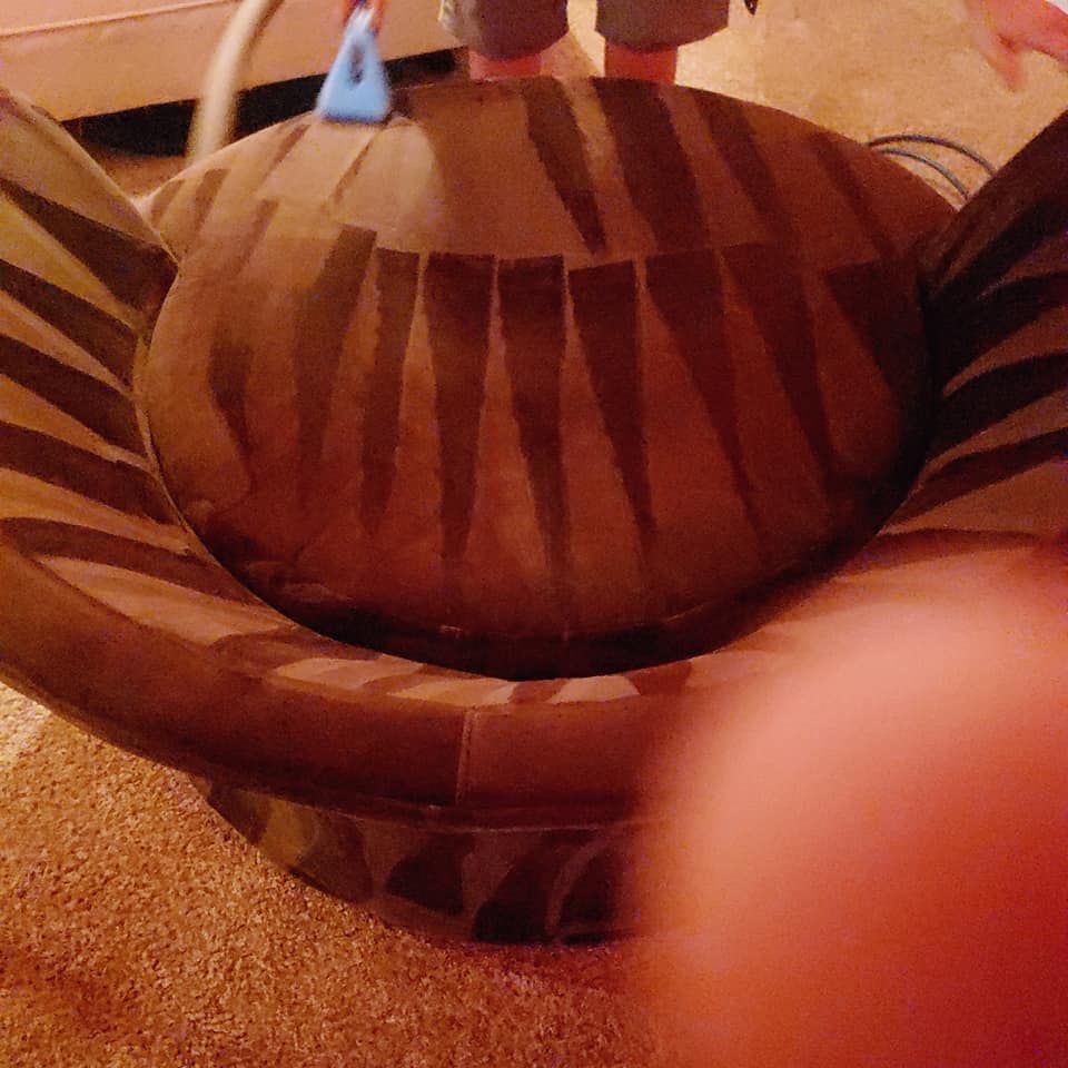 A person uses a cleaning tool on a round, brown chair featuring vertical stripe patterns on its cushion and base.