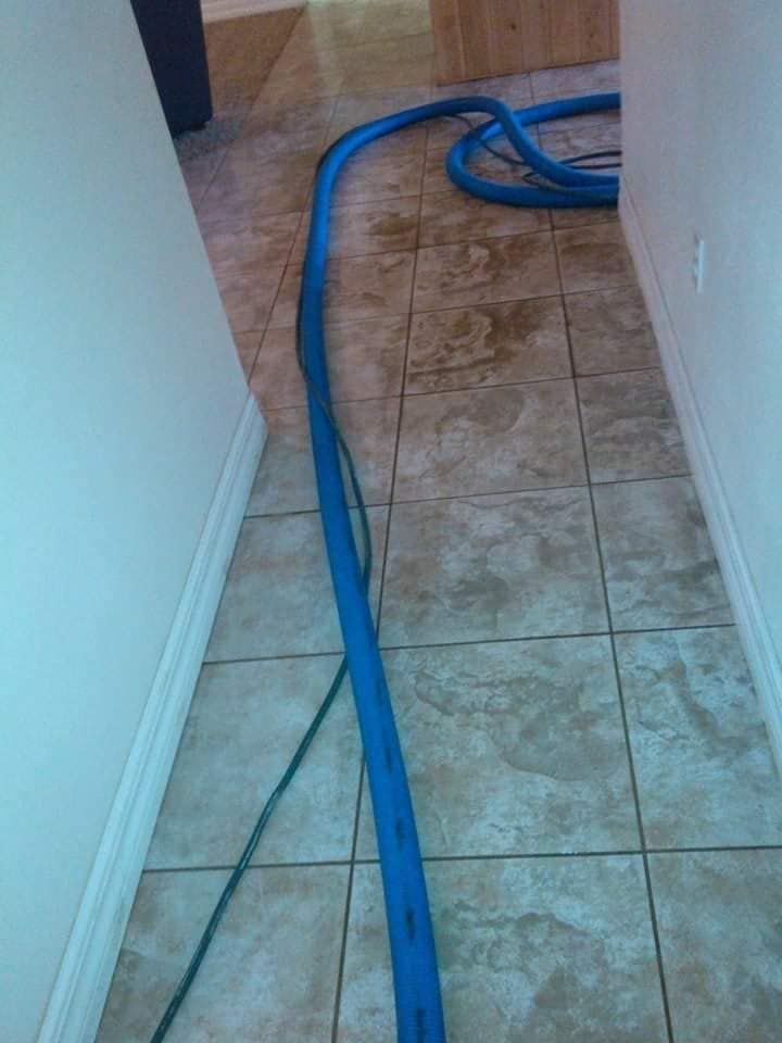 A long, blue vacuum hose lies across a tiled floor in a narrow hallway.