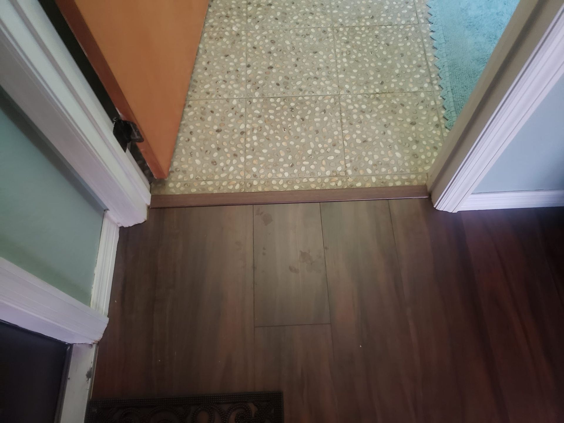 A transition strip separates a dark brown wood-look floor from a room with light, speckled square tiles.