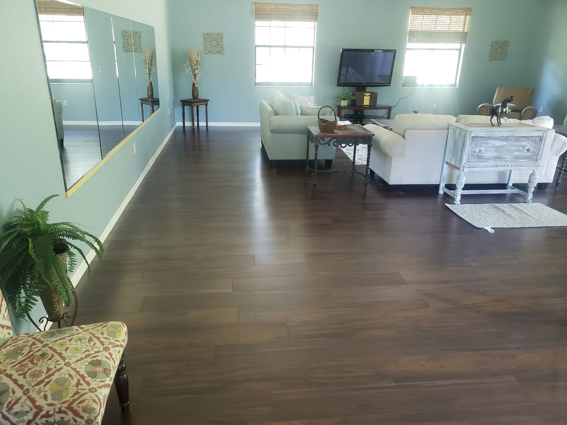 A spacious, open-plan living room with dark wood floors, light blue walls, a white sofa, and large wall mirrors.