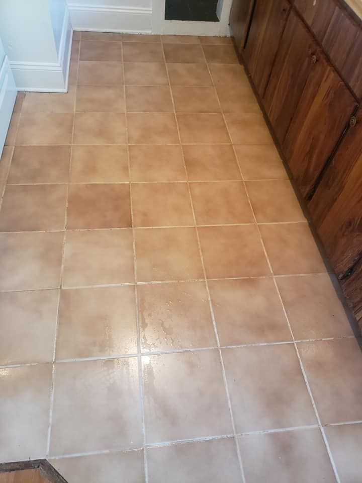 A floor covered in square, light brown mottled tiles next to dark wood cabinets.