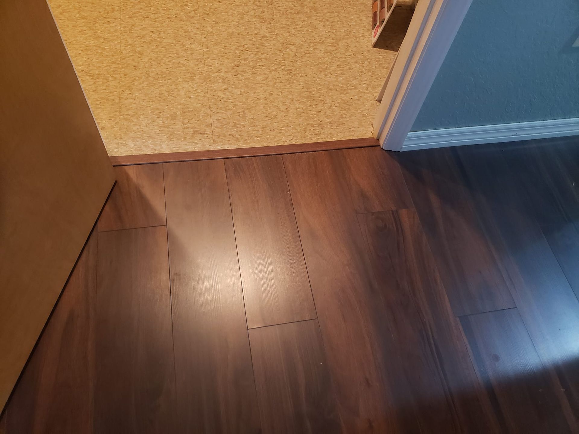A transition strip separates a dark brown wood-look laminate floor from a carpeted room at a doorway.
