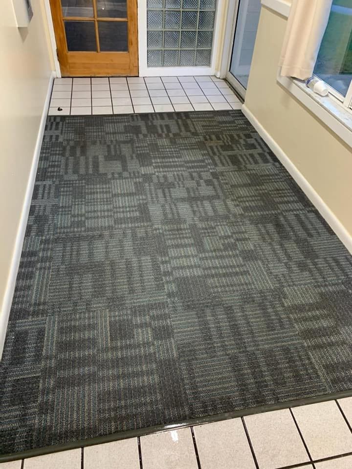 A grey, textured carpet runner centered on a tiled hallway floor leading toward a glass-paned wooden door.