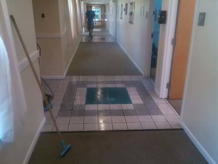 A person walks down a hallway with beige walls, featuring a section of patterned, square tiles on the floor.