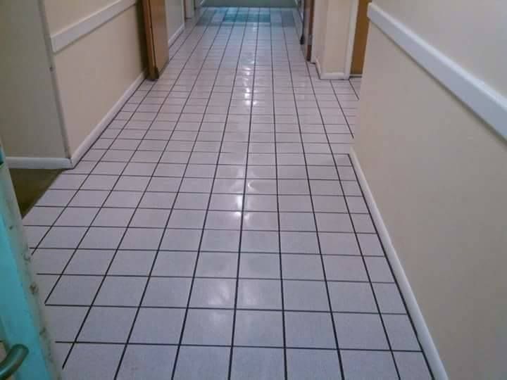 A hallway with light-colored square floor tiles, white walls, and a door visible at the end of the corridor.