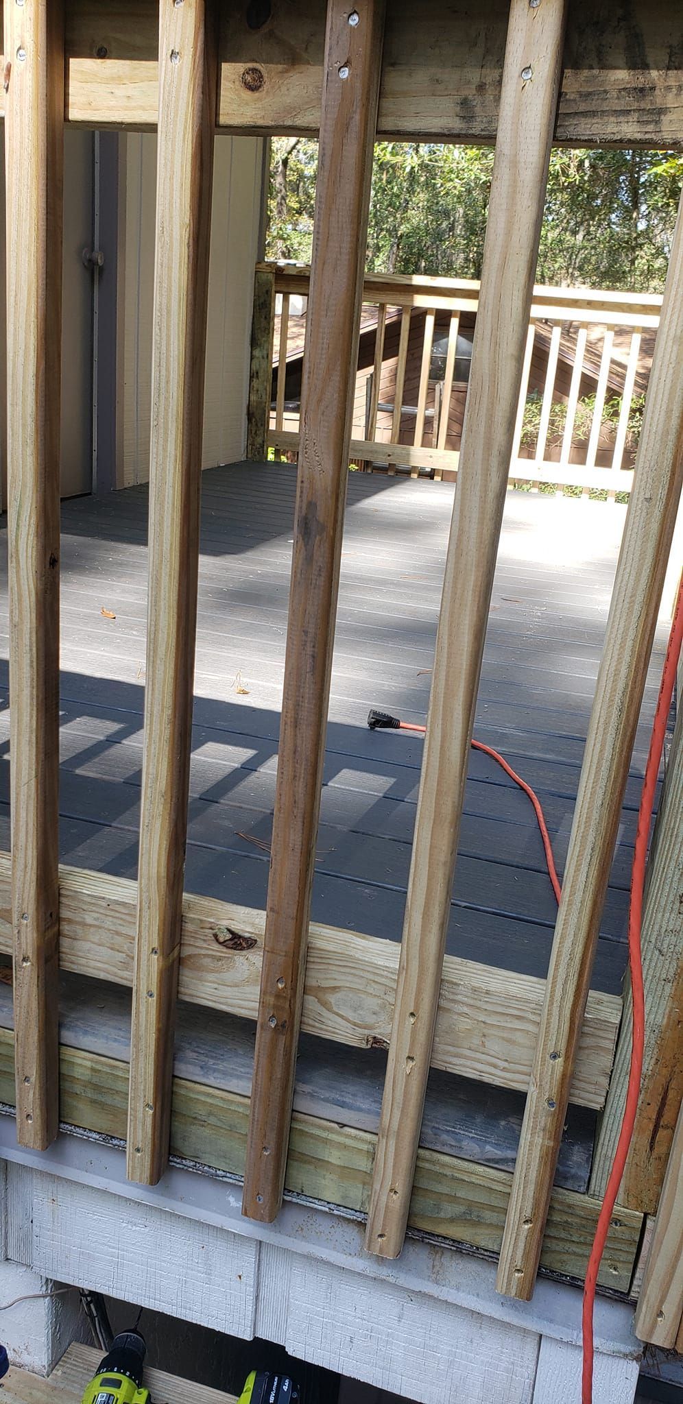 Wooden porch railing in the foreground looking over a deck with black interlocking floor tiles.