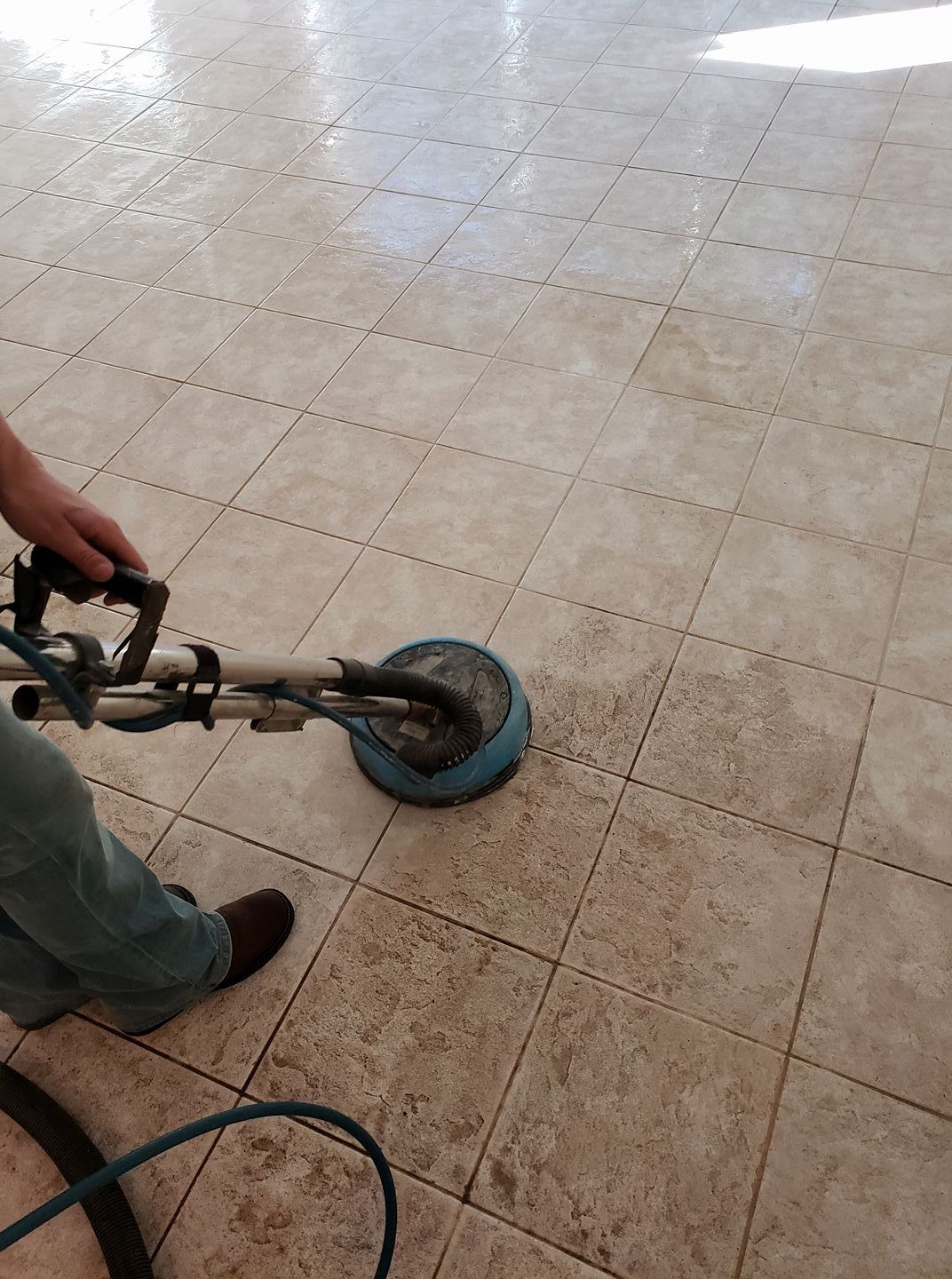 A person uses a floor cleaning machine on a tiled surface, showing a clear contrast between dirty and clean tiles.
