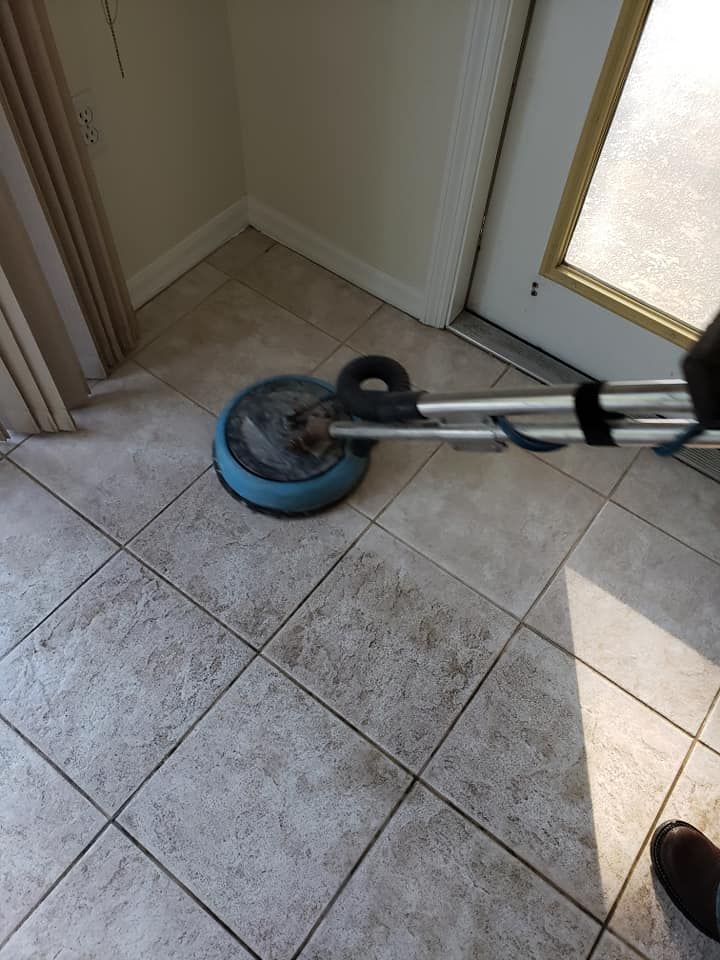 A floor cleaning machine scrubbing light-colored tiled floors near a corner and a doorway.