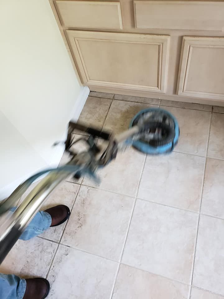 A person uses a floor buffer to clean tiled bathroom flooring in front of cabinets.