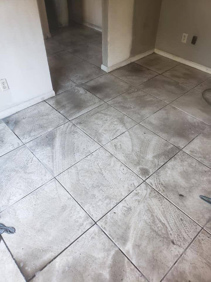 A room with light-colored, square floor tiles showing significant gray haze and construction dust residue.