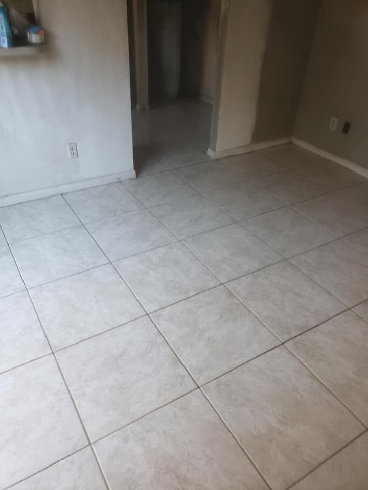 A floor covered in light beige, square ceramic tiles with a textured pattern, leading toward a dark doorway.
