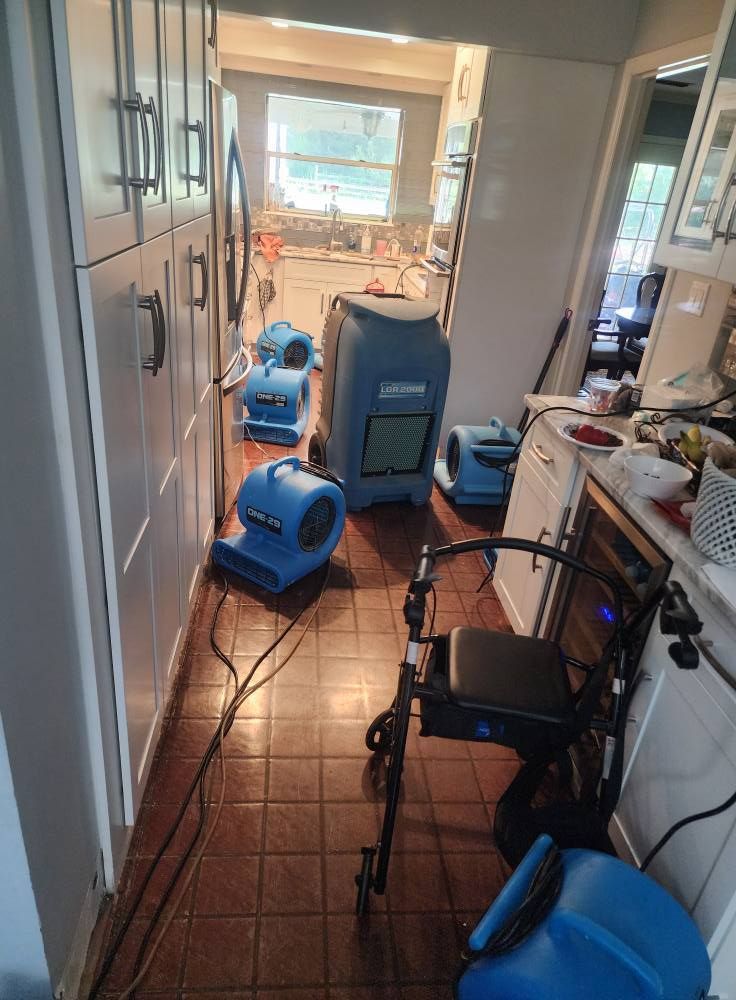 Blue industrial air movers and a large dehumidifier placed on a tiled kitchen floor during water damage restoration.