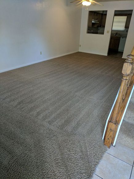 A room with beige wall-to-wall carpeting and neutral walls, viewed from a slightly elevated entryway.