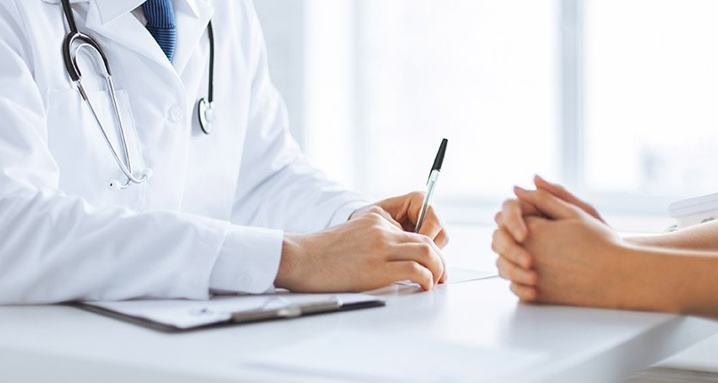 A doctor is sitting at a desk talking to a patient.