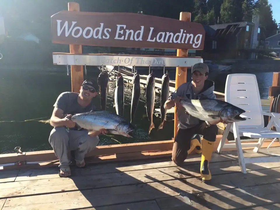 Two men holding fish in front of a sign that says woods end landing