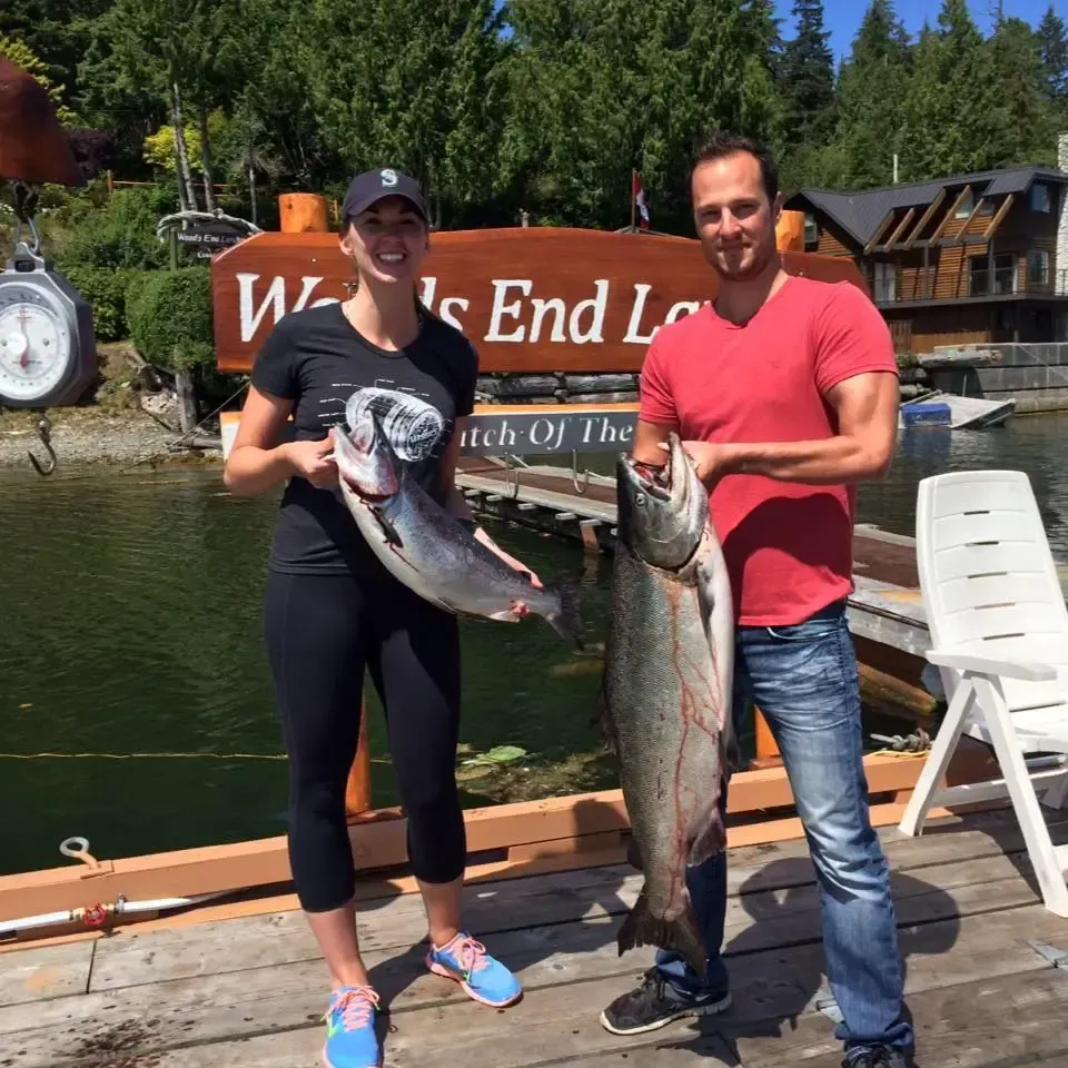 A man and a woman are holding a large fish in front of a sign that says welcome to the end