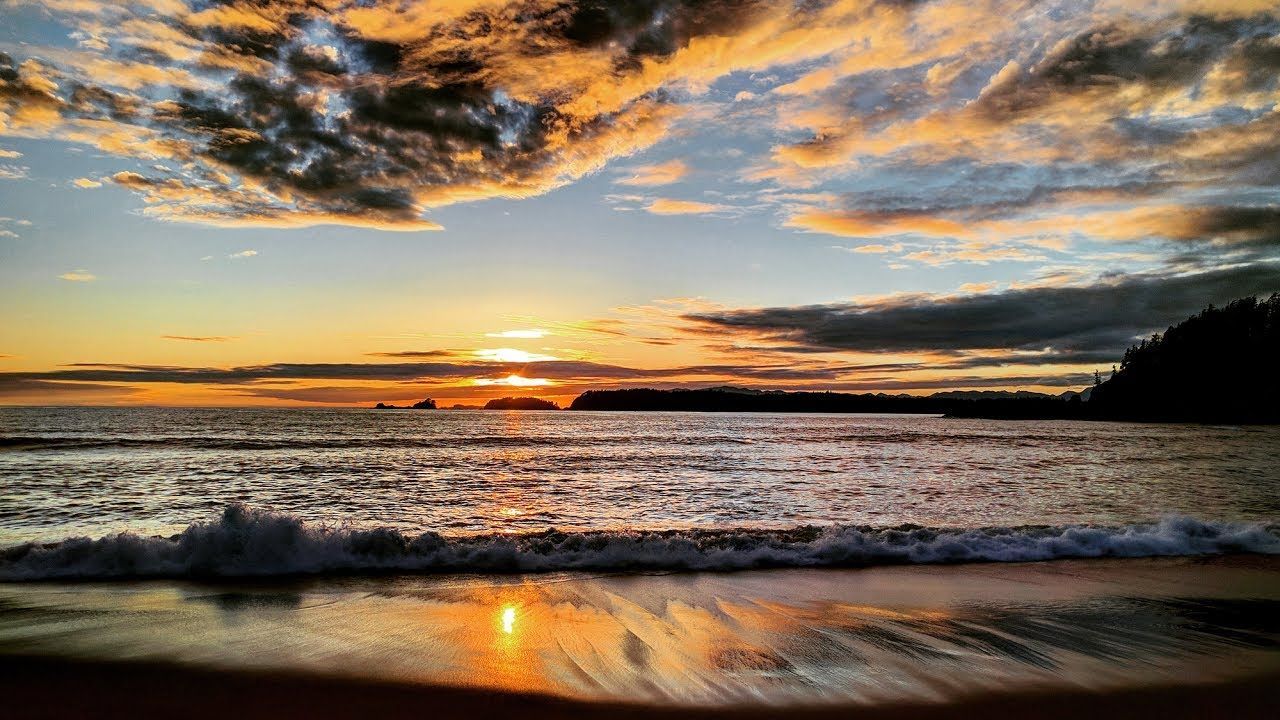 The sun is setting over the ocean and the waves are crashing on the beach.