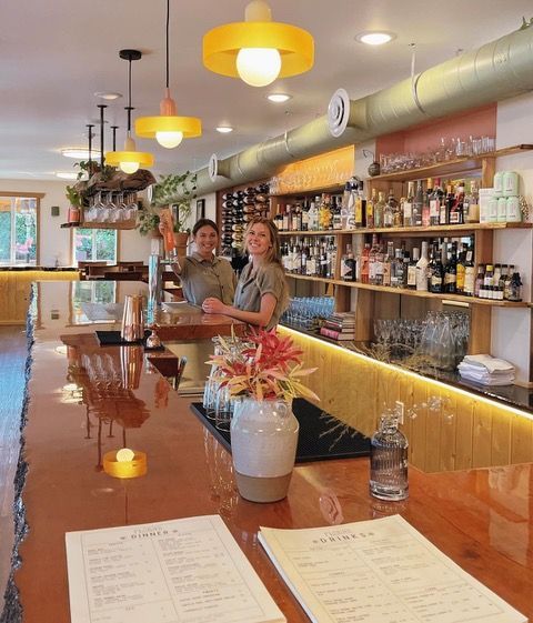 Two women are standing behind a bar in a restaurant