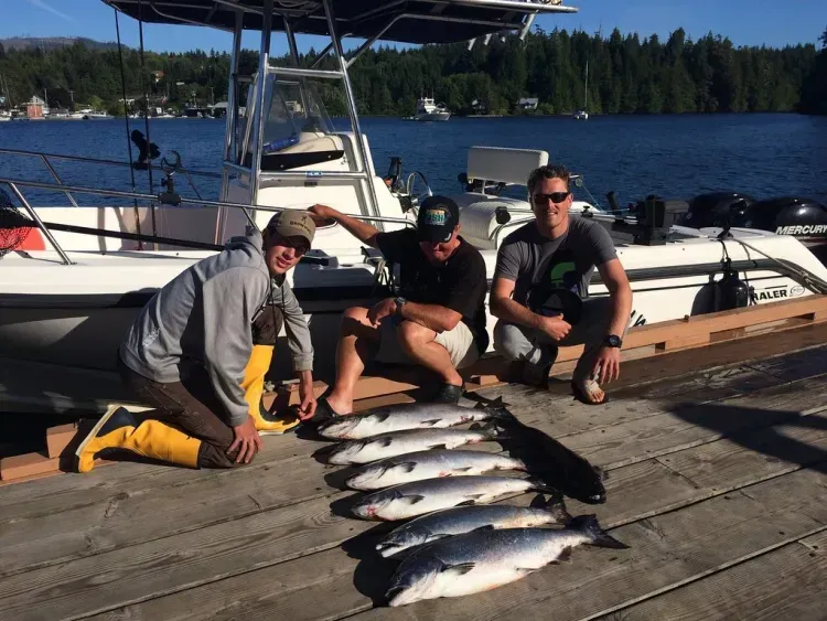 Three men are kneeling on a dock with a bunch of fish