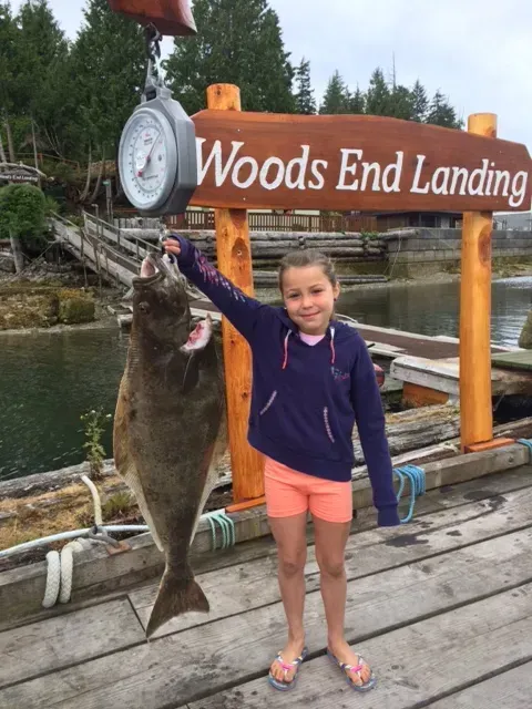 A little girl is holding a large fish in front of a sign that says woods end landing