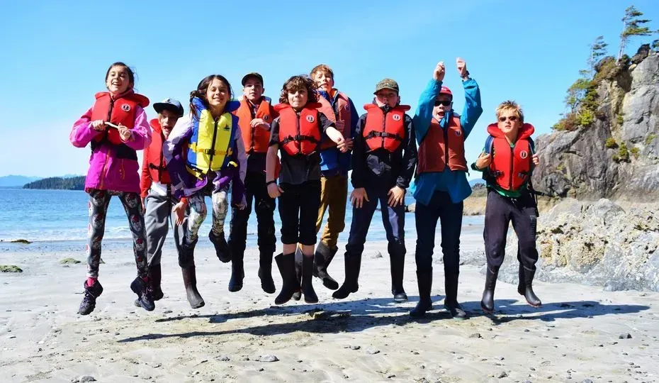 A group from Bamfield Marine Science Center are jumping in the air on a beach.
