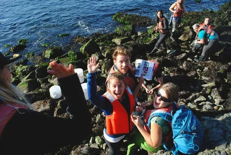 A group of students are standing on a rocky shoreline near the water at Bamfield Marine Science Center in Bamfield