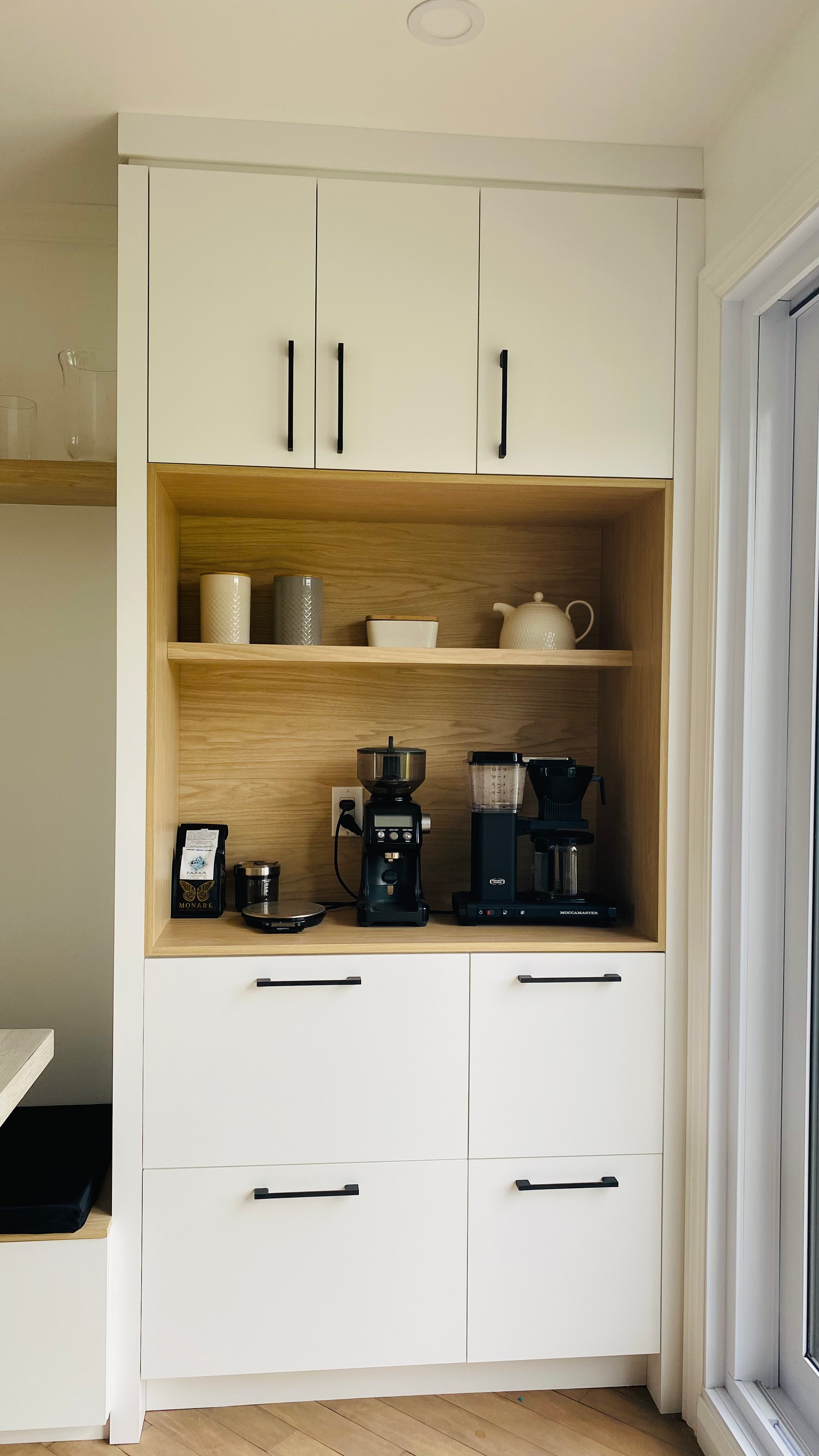 Coin café avec placards blancs, touches de bois clair, cafetière et moulin à café.