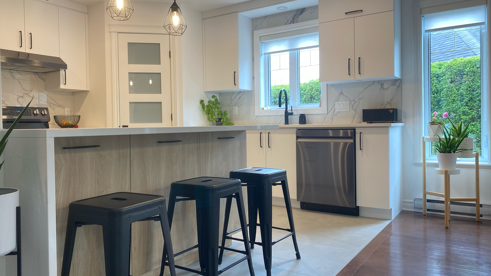 Cuisine moderne avec armoires blanches, appareils électroménagers en acier inoxydable et tabourets noirs à l'îlot central.