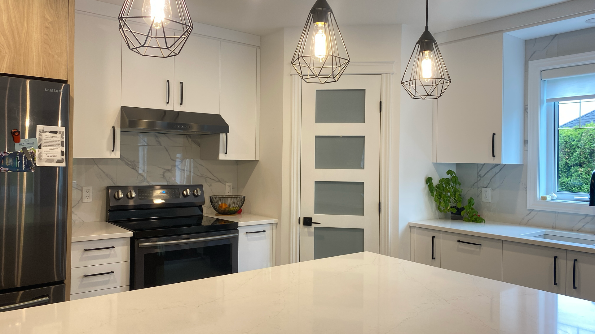 Cuisine blanche moderne avec îlot central, cuisinière et luminaires suspendus.