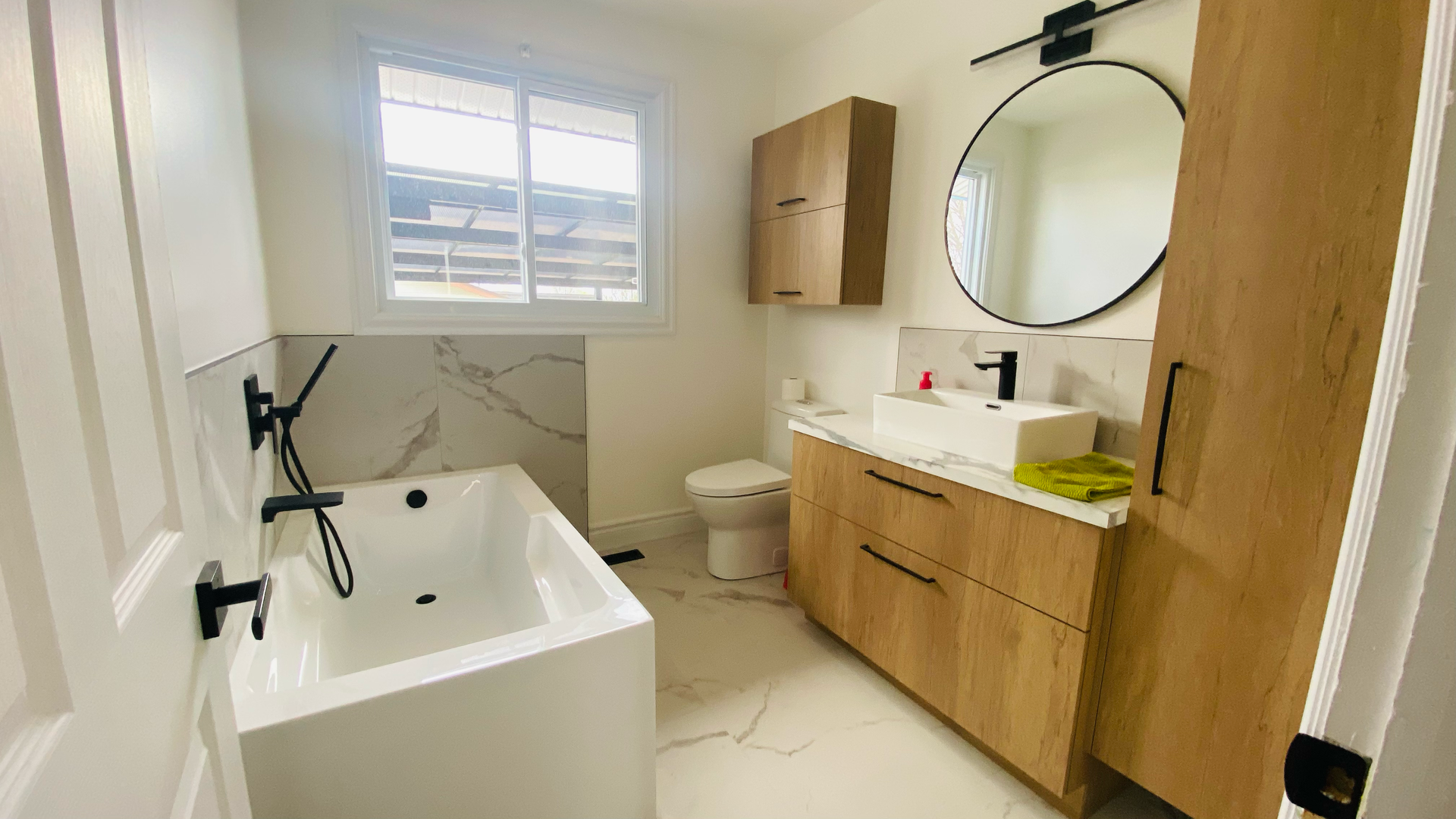 Salle de bains moderne avec baignoire blanche, meuble-lavabo en bois et miroir rond.