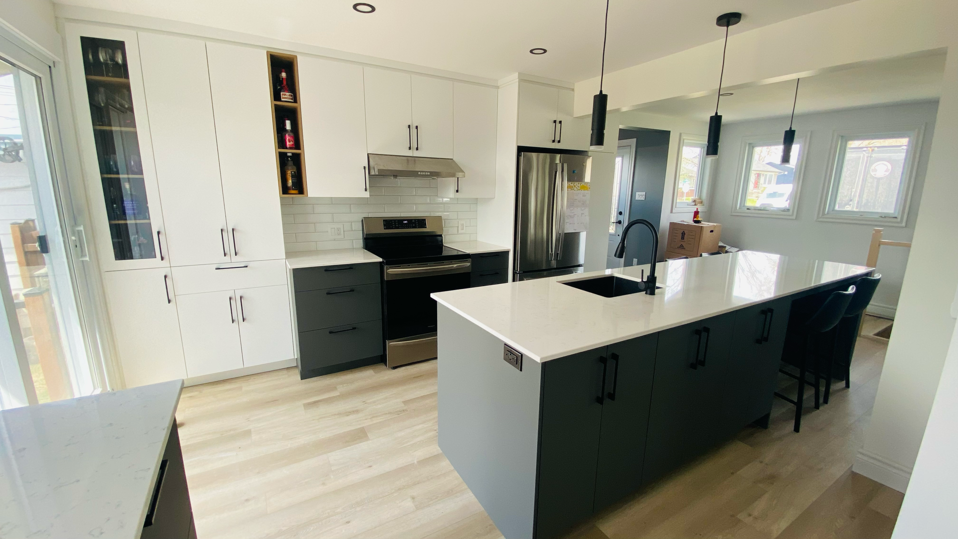 Cuisine moderne avec armoires blanches et grises, îlot central, appareils électroménagers en acier inoxydable et plancher en bois.