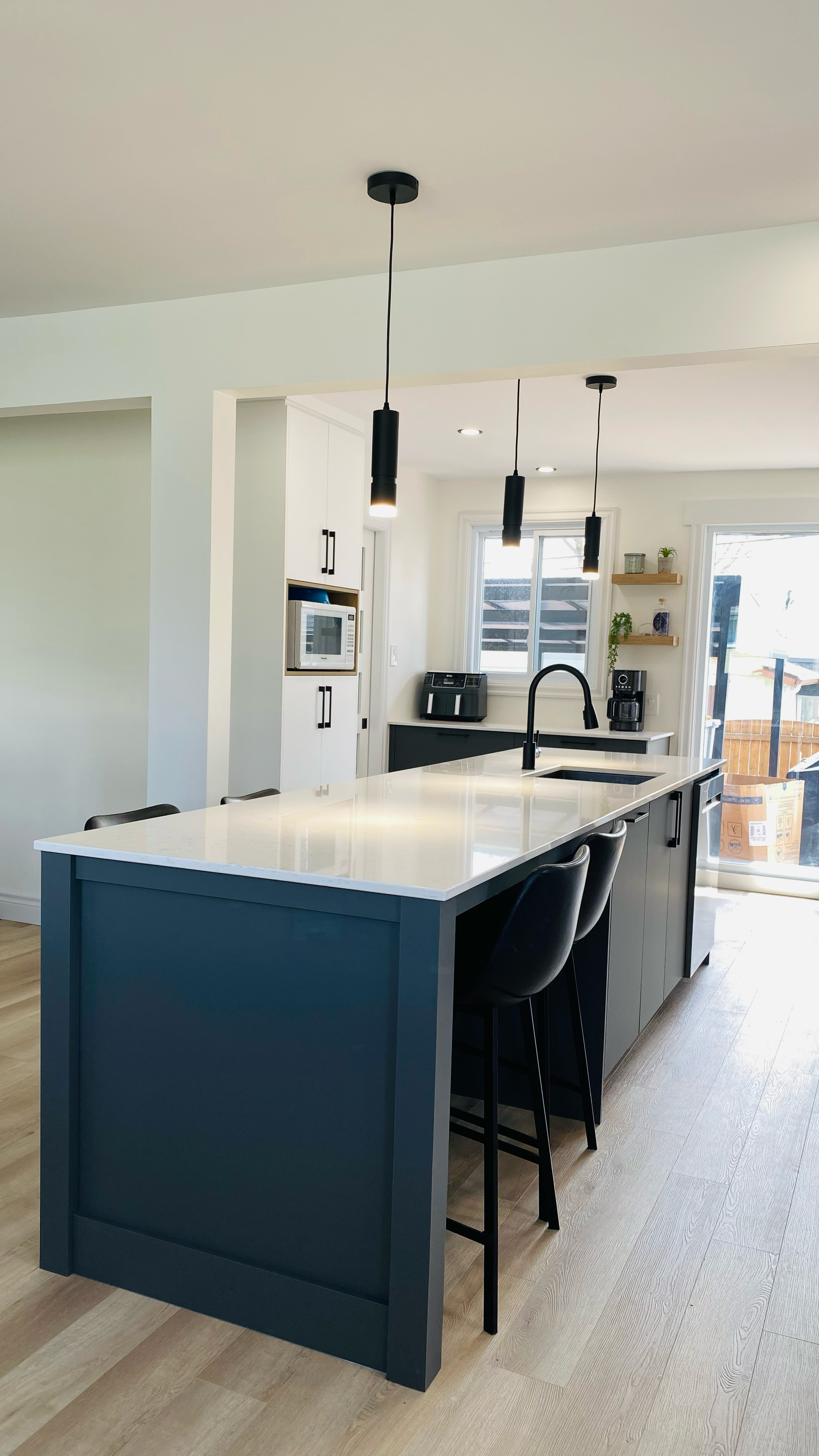 Cuisine moderne avec îlot bleu, plan de travail blanc, tabourets noirs et suspensions lumineuses.