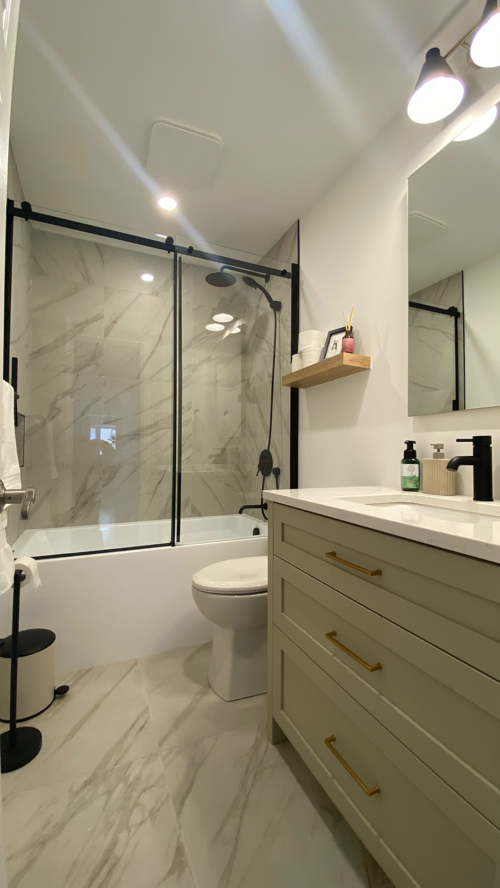 Salle de bains avec carrelage en marbre blanc, cadre de douche noir et meuble-lavabo vert clair.