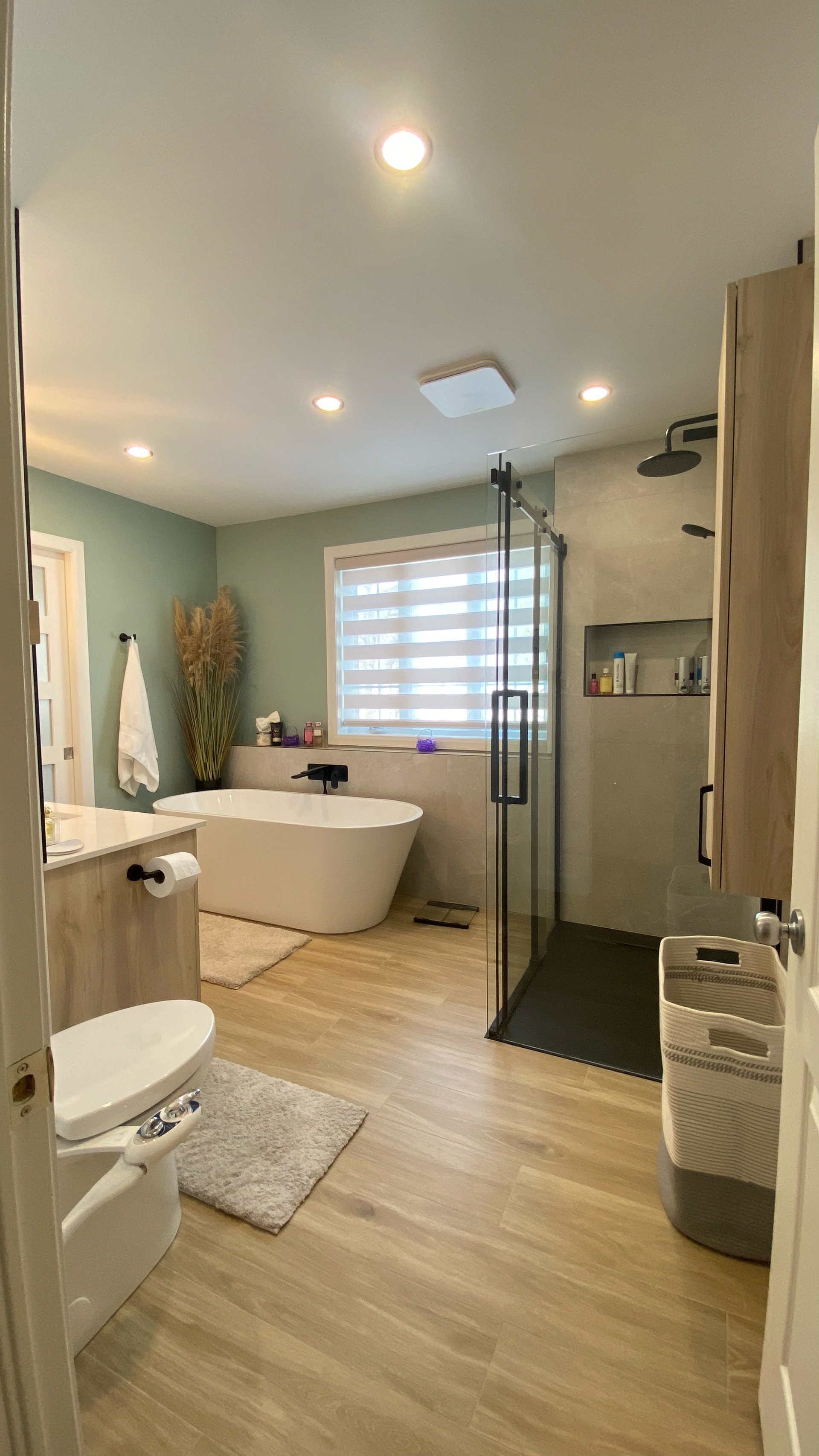 Salle de bains moderne avec baignoire îlot, douche en verre et parquet clair.