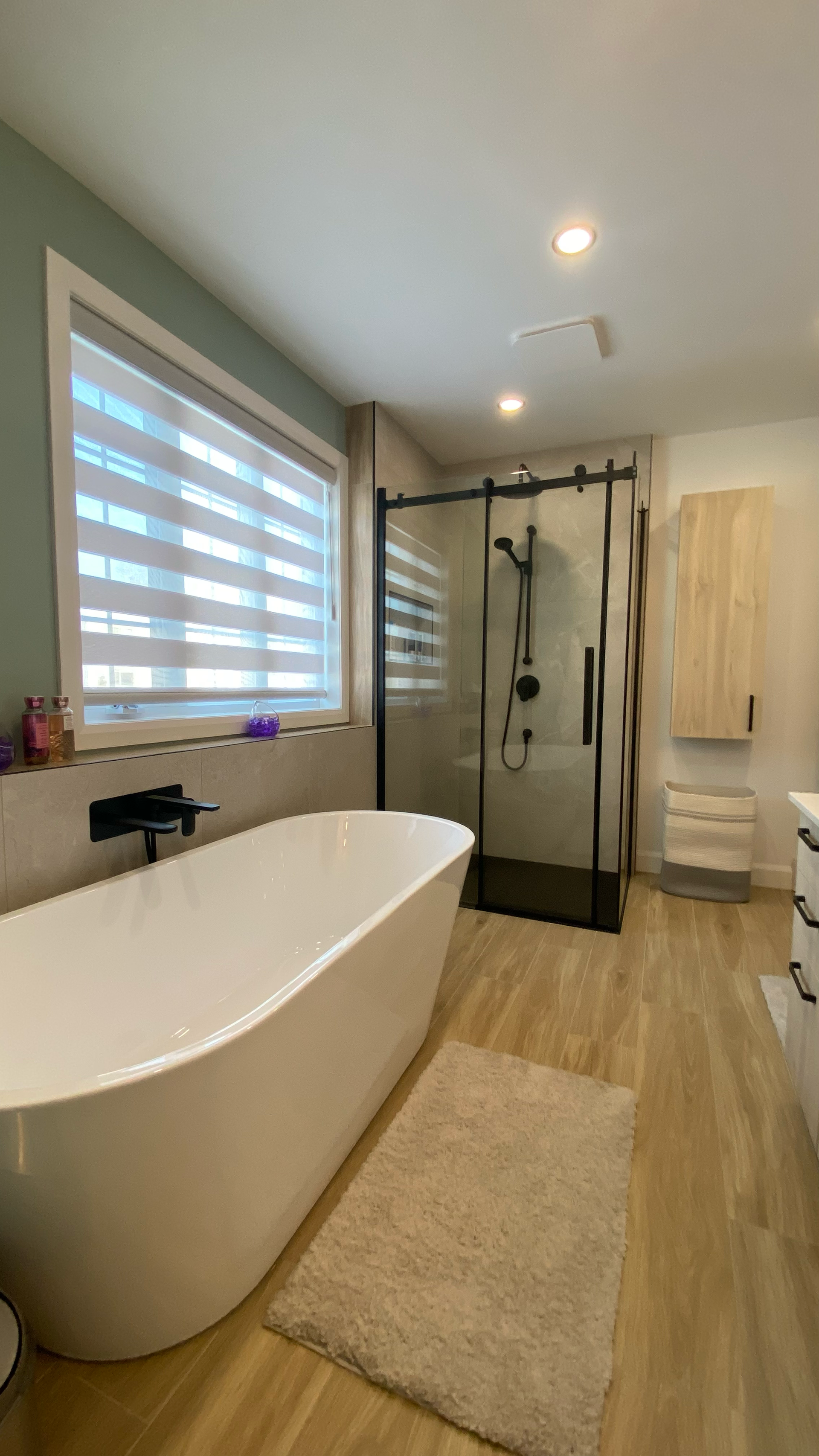 Salle de bains moderne avec baignoire blanche, douche en verre, parquet clair et tapis moelleux.