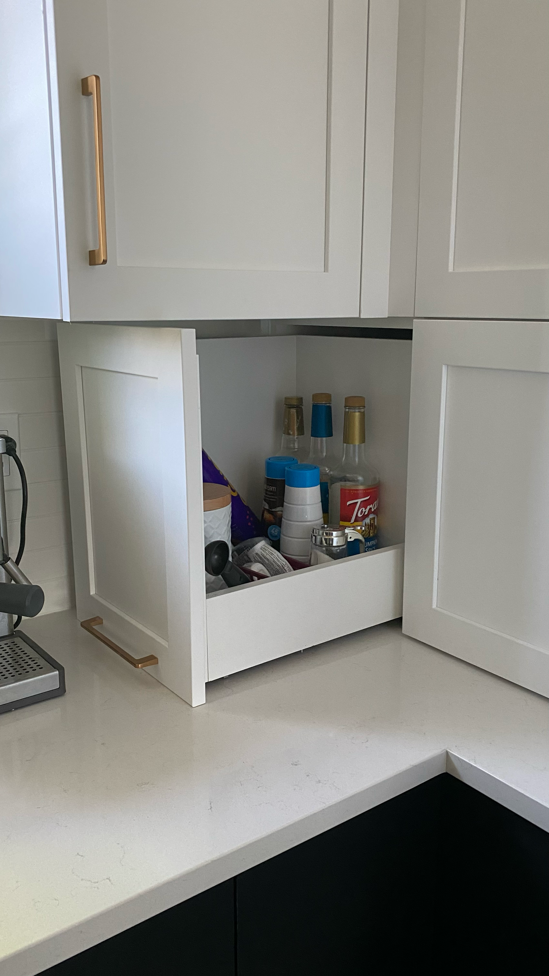 Meuble de cuisine blanc avec une étagère coulissante contenant des bouteilles et des objets sur le plan de travail.