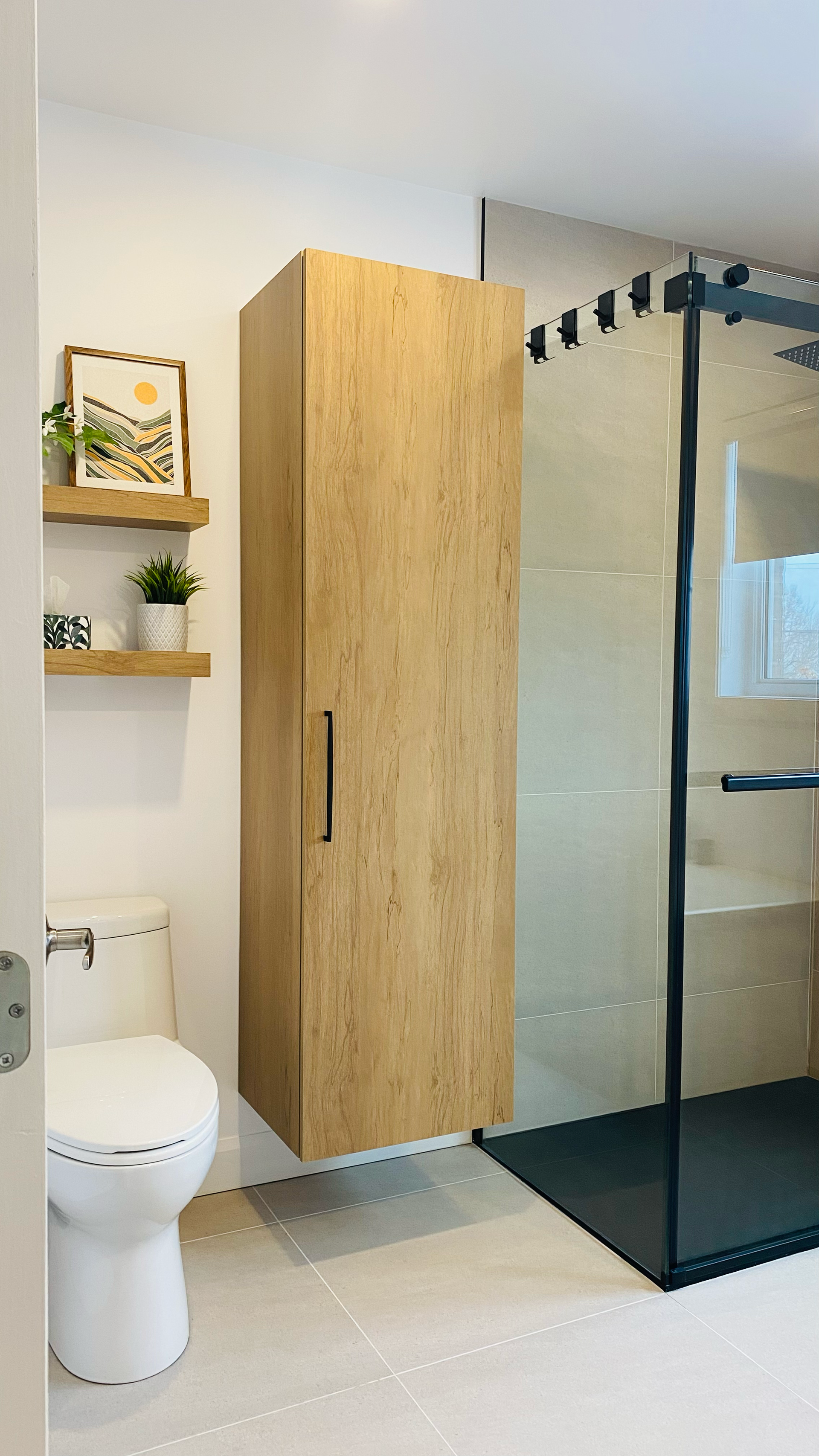 Salle de bains avec meuble en bois, douche ouverte avec porte en verre et étagères suspendues.