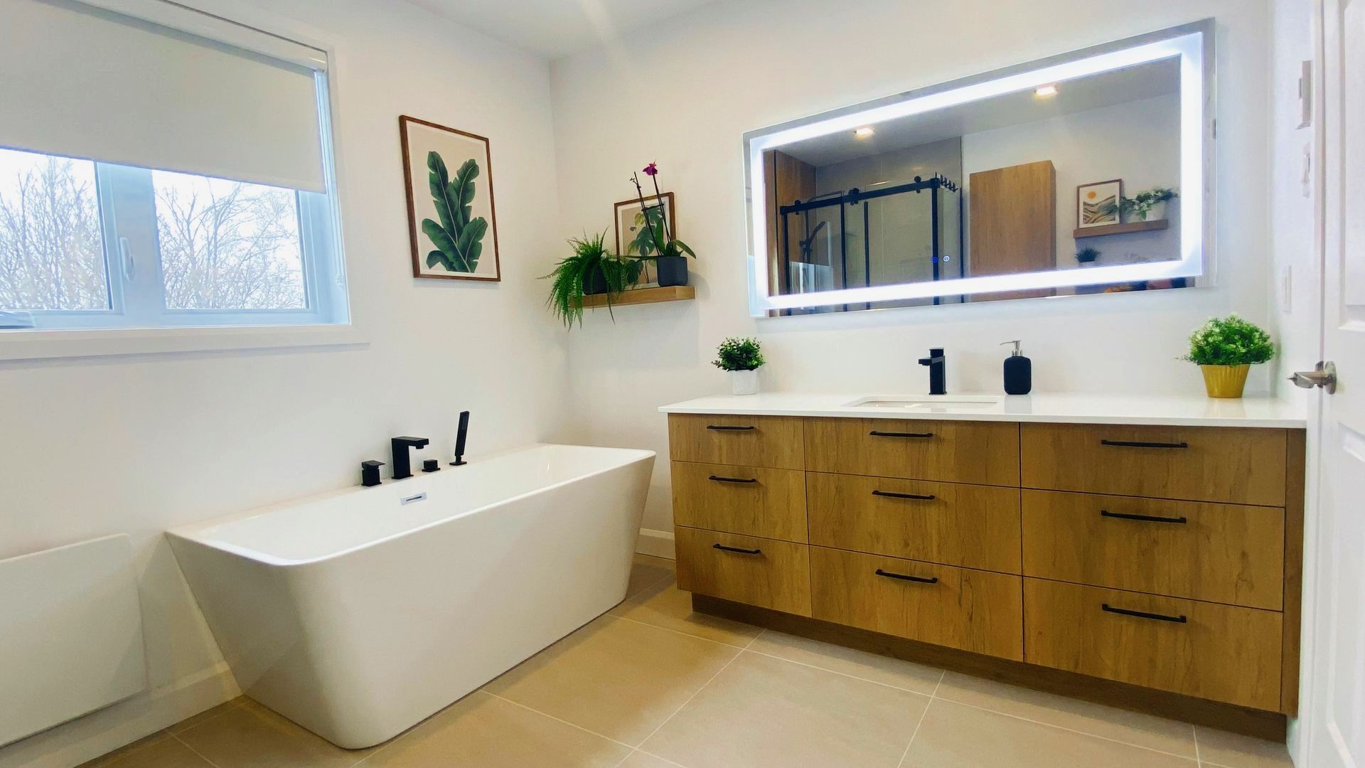 Salle de bains moderne avec meuble-lavabo en bois, grand miroir, baignoire îlot et petites plantes.