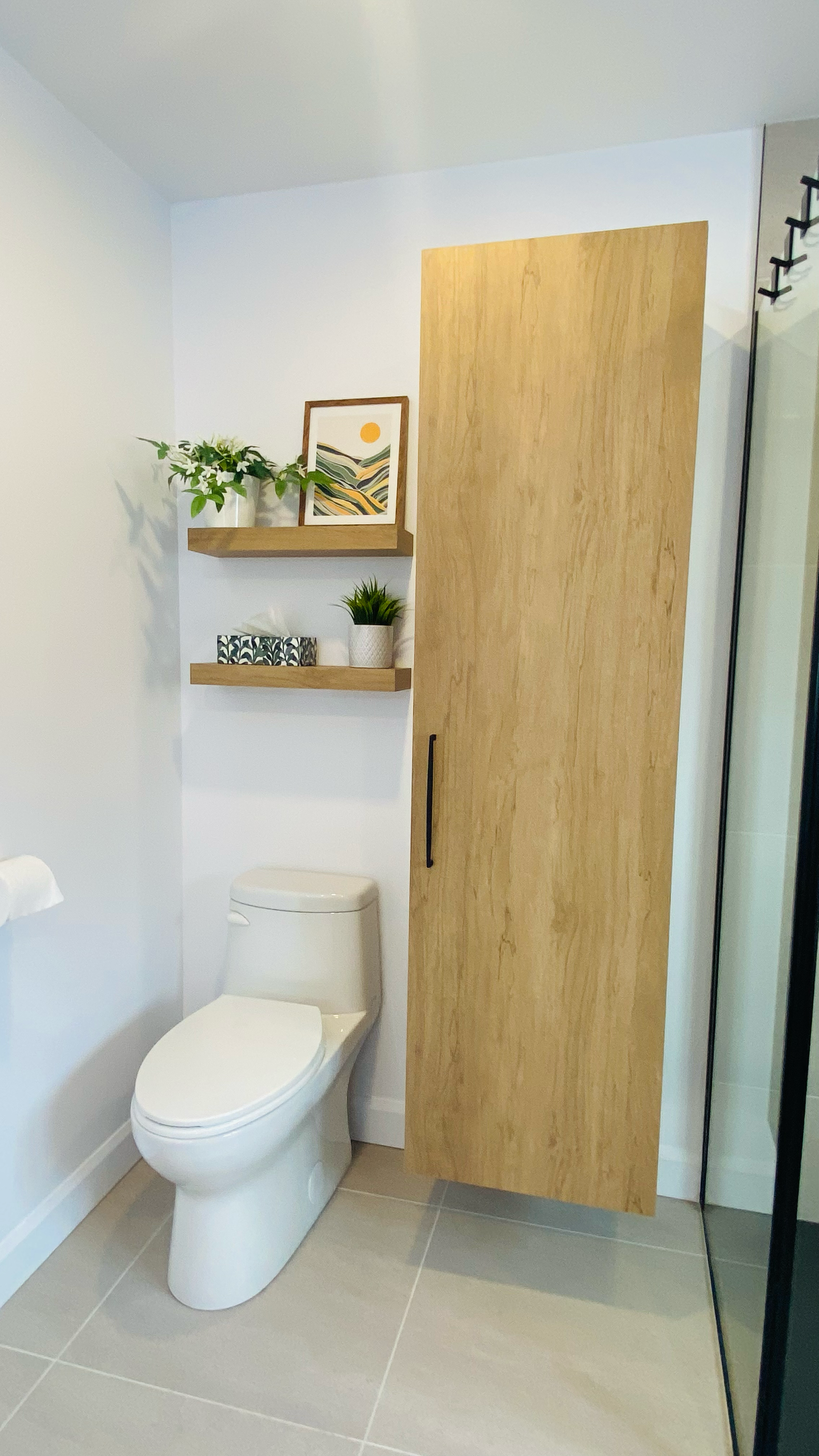 Salle de bains avec toilettes, meuble de rangement en bois, étagères flottantes avec plantes et œuvres d'art.