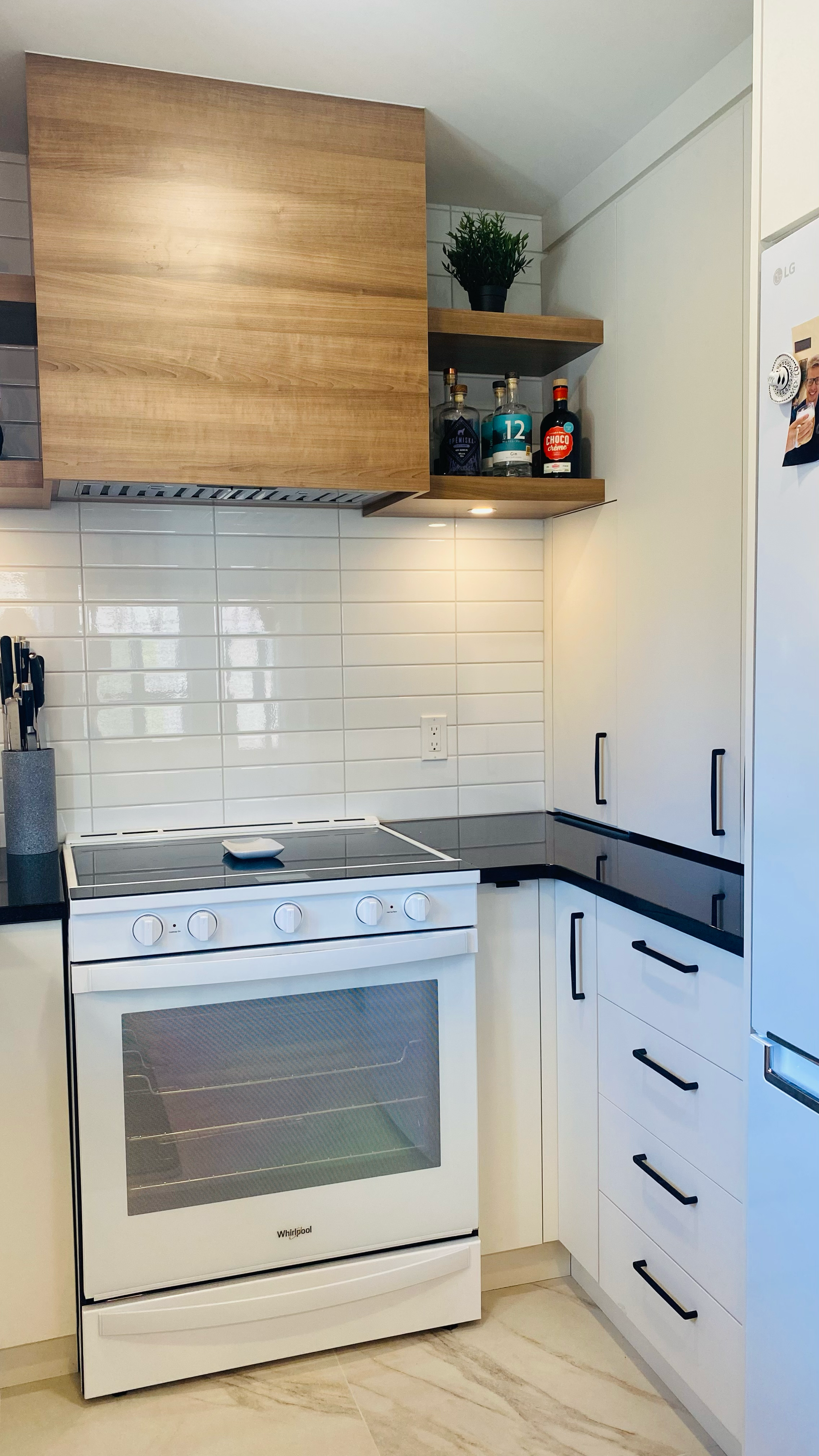 Cuisine blanche avec cuisinière, hotte en bois, étagères ouvertes et placards blancs.