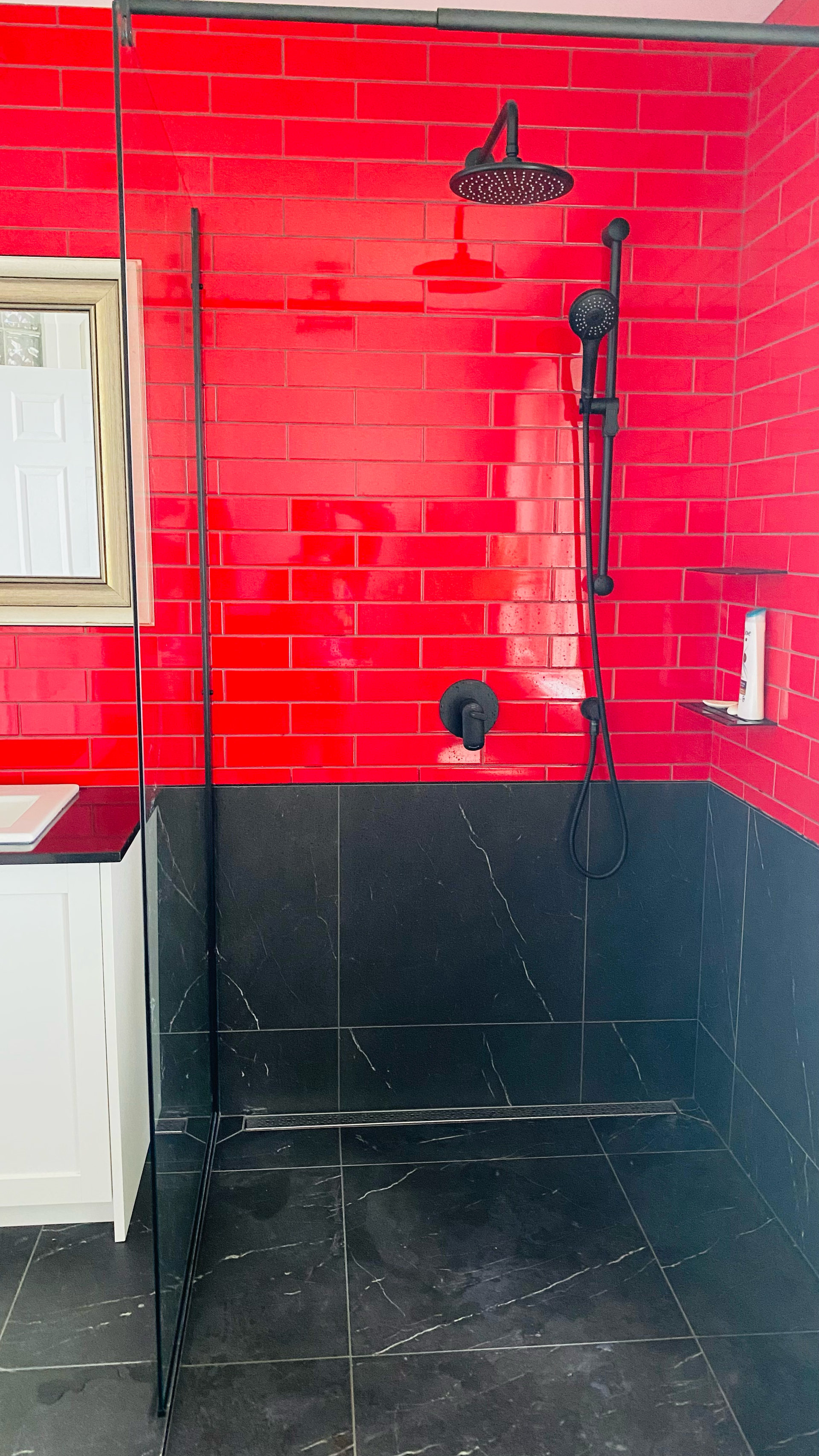 Douche carrelée rouge et noire avec robinetterie noire et fenêtre.