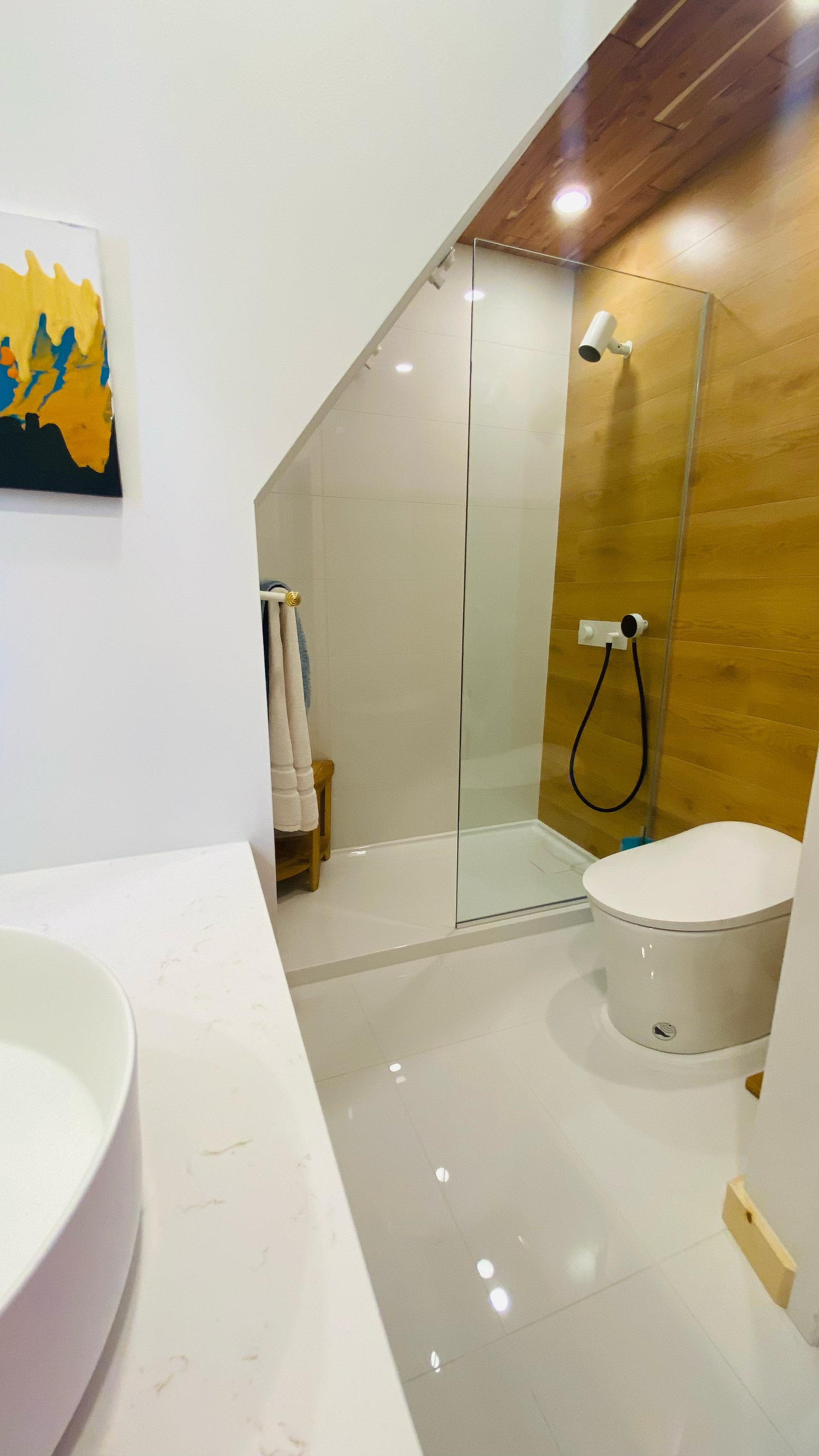 Salle de bains moderne avec des touches de blanc et de bois ; douche en verre, toilettes et lavabo.