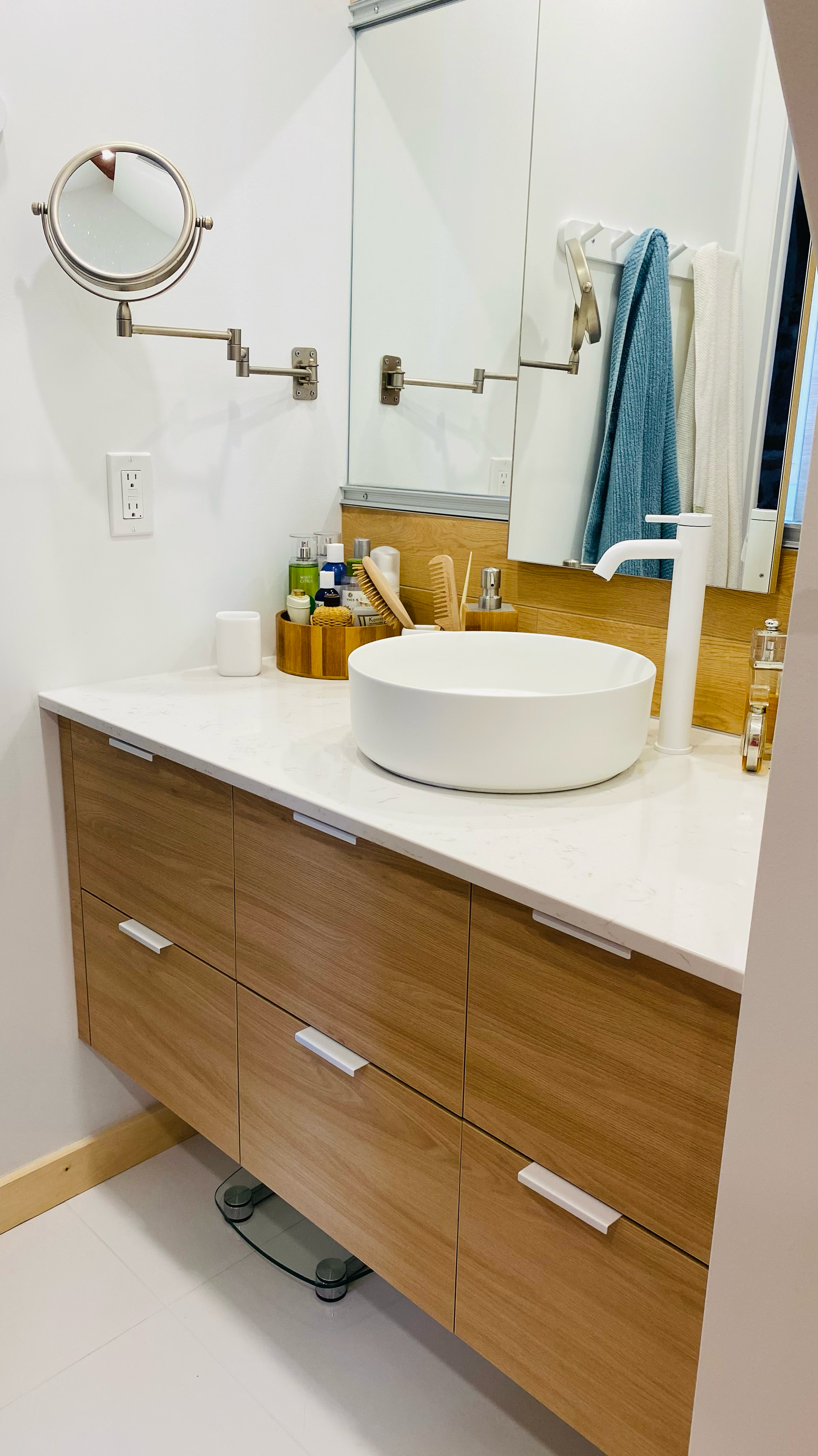Salle de bains avec meuble-lavabo en bois, comptoir blanc, lavabo rond, miroir et serviettes.