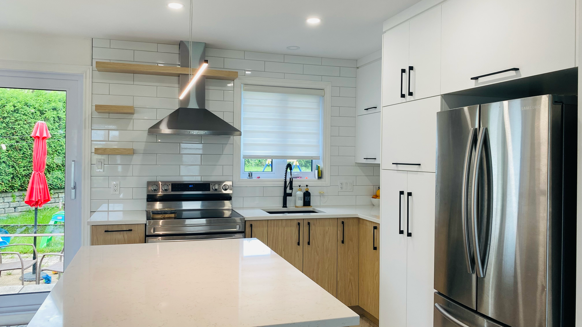 Cuisine moderne avec électroménagers en acier inoxydable, armoires blanches, accents de bois clair et îlot central.
